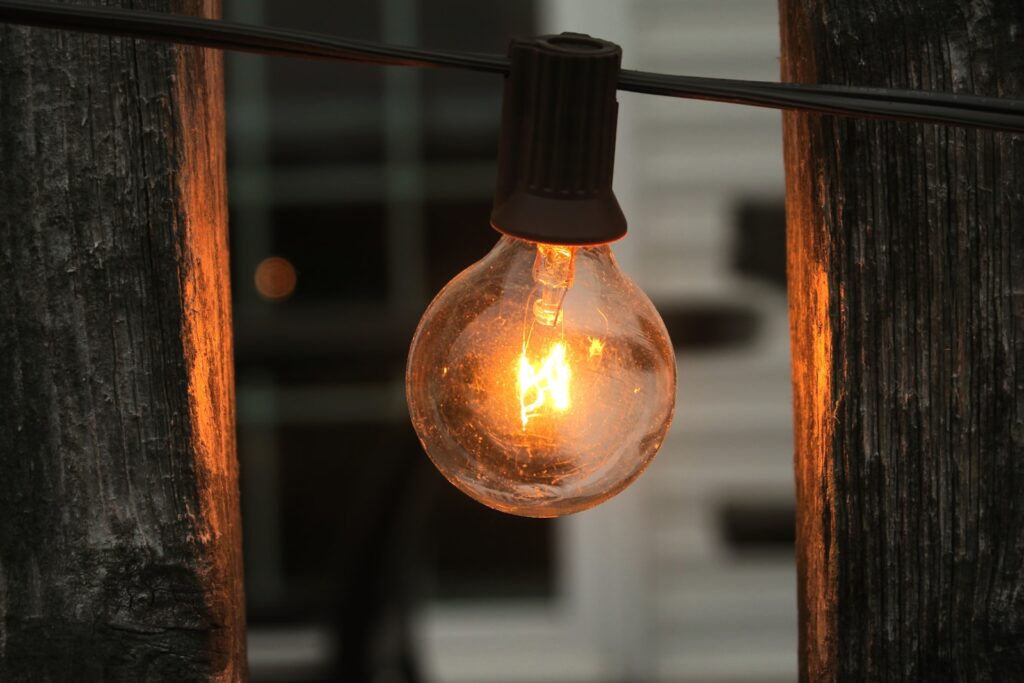 A light bulb hanging from a wire with a house in the background